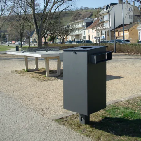 Öffentlicher Abfallbehälter aus Stahl mit minimalistischer Formgebung in einem Parkumfeld