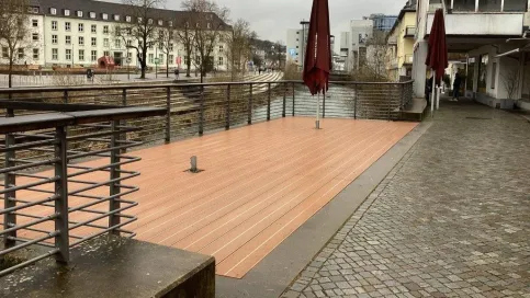 Holzterrasse mit Edelstahlgeländer am Wasser, umgeben von Pflastersteinen