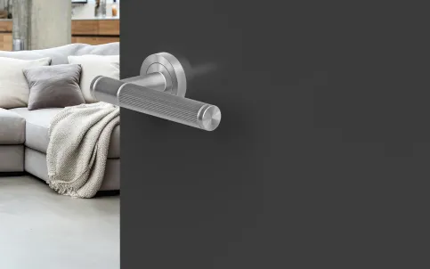 KD Basic Studio Serie | Verschließtechnik im Vierkantstift Türgriff aus Edelstahl an einer modernen, mattschwarzen Tür mit Sicht auf einen minimalistischen Wohnraum