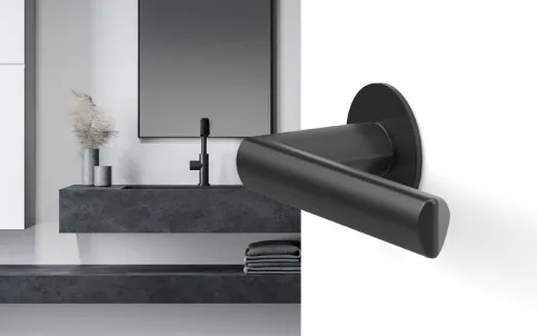 Plan Design Paris | runde Rosette, aufgesetzt montiert, Farbe Kosmos Schwarz Schwarzer Türgriff aus Metall an einer minimalistischen Wand mit Waschbecken und Spiegel